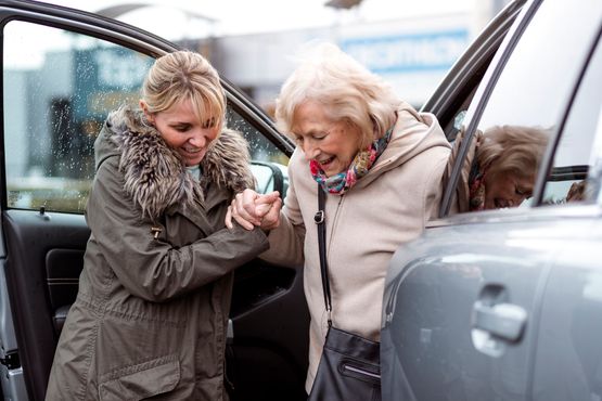 blonde-Frau-stuetzt-aeltere-Dame-und-hilft-ihr-aus-einem-Fahrzeug-auszusteigen