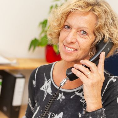 Frau-mit-blonden-kurzen-Haaren-sitzt-im-Buero-und-telefoniert